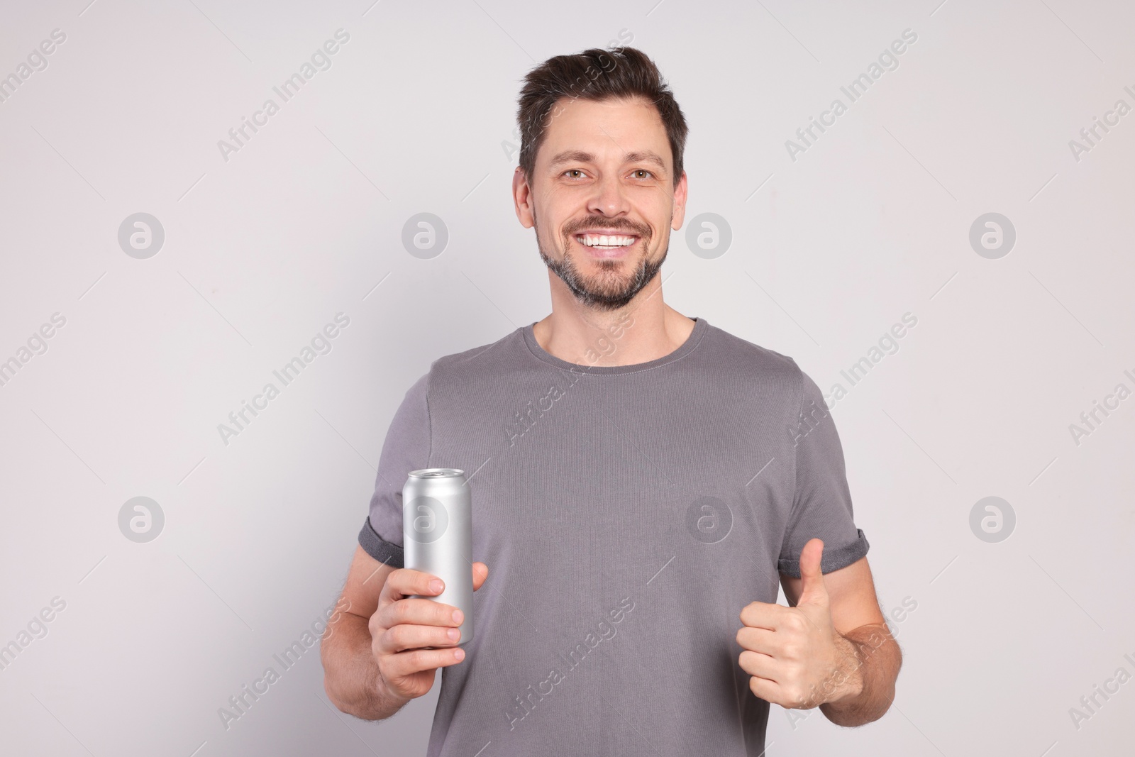 Photo of Happy man holding tin can with beverage on light grey background