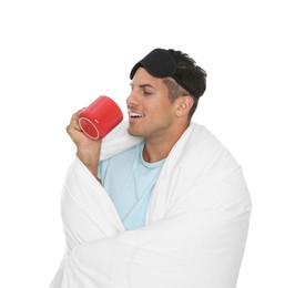 Man in sleeping mask wrapped with blanket holding cup on white background