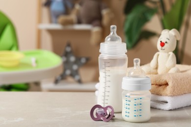 Photo of Feeding bottles with baby formula, pacifier and towels on light grey table indoors. Space for text