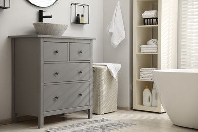 Stylish bathroom interior with grey chest of drawers and shelving unit