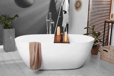 Photo of Stylish bathroom interior with ceramic tub, cosmetic products and houseplants
