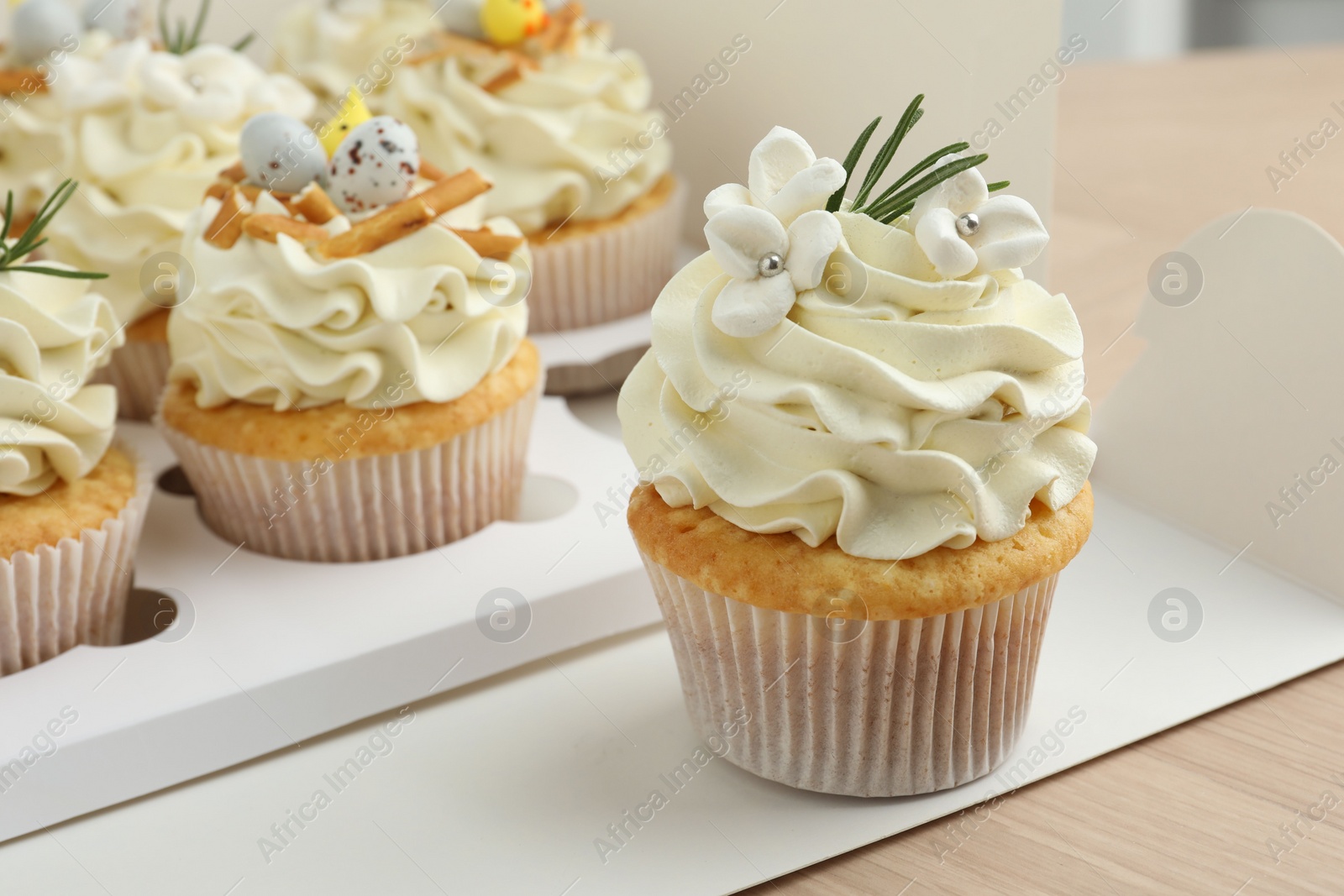 Photo of Tasty Easter cupcakes in box on wooden table, closeup