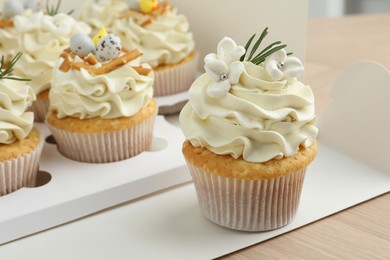 Tasty Easter cupcakes in box on wooden table, closeup