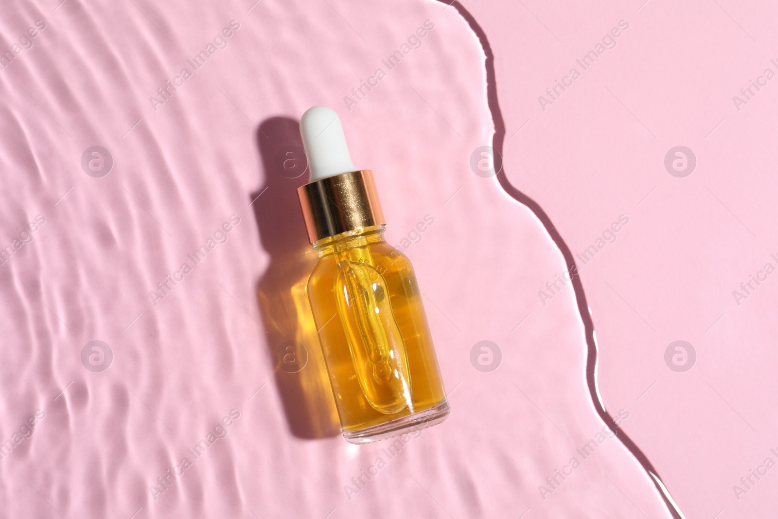 Photo of Bottle of cosmetic oil in water on pink background, top view