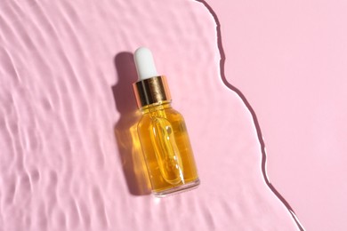 Bottle of cosmetic oil in water on pink background, top view