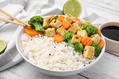Bowl of rice with fried tofu, broccoli and carrots on white wooden table, closeup