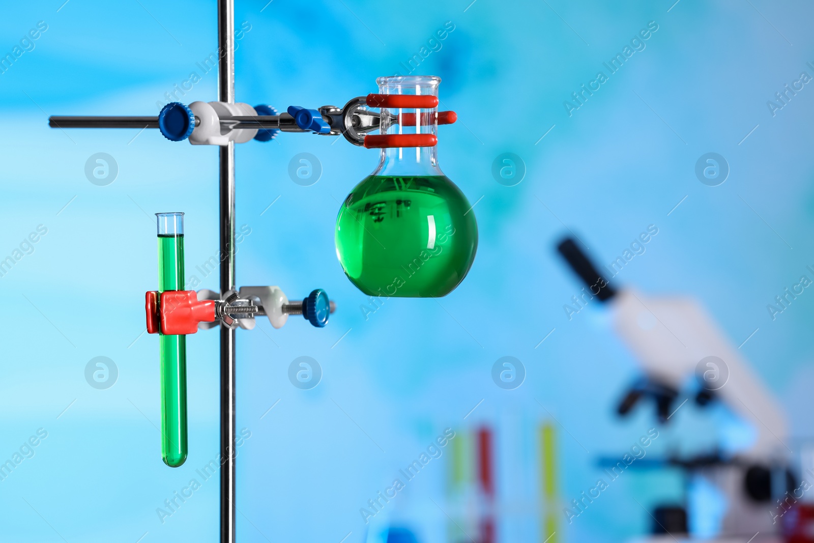 Photo of Laboratory glassware with green liquid on retort stand indoors. Space for text