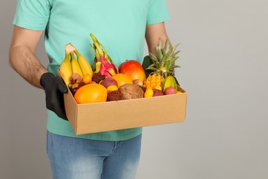 Photo of Courier holding box with assortment of exotic fruits on grey background, closeup
