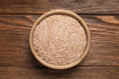 Photo of Bowl of wheat bran on wooden table, top view