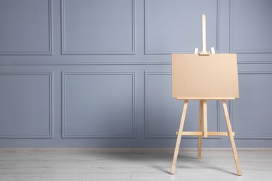 Wooden easel with blank board near grey wall indoors. Space for text