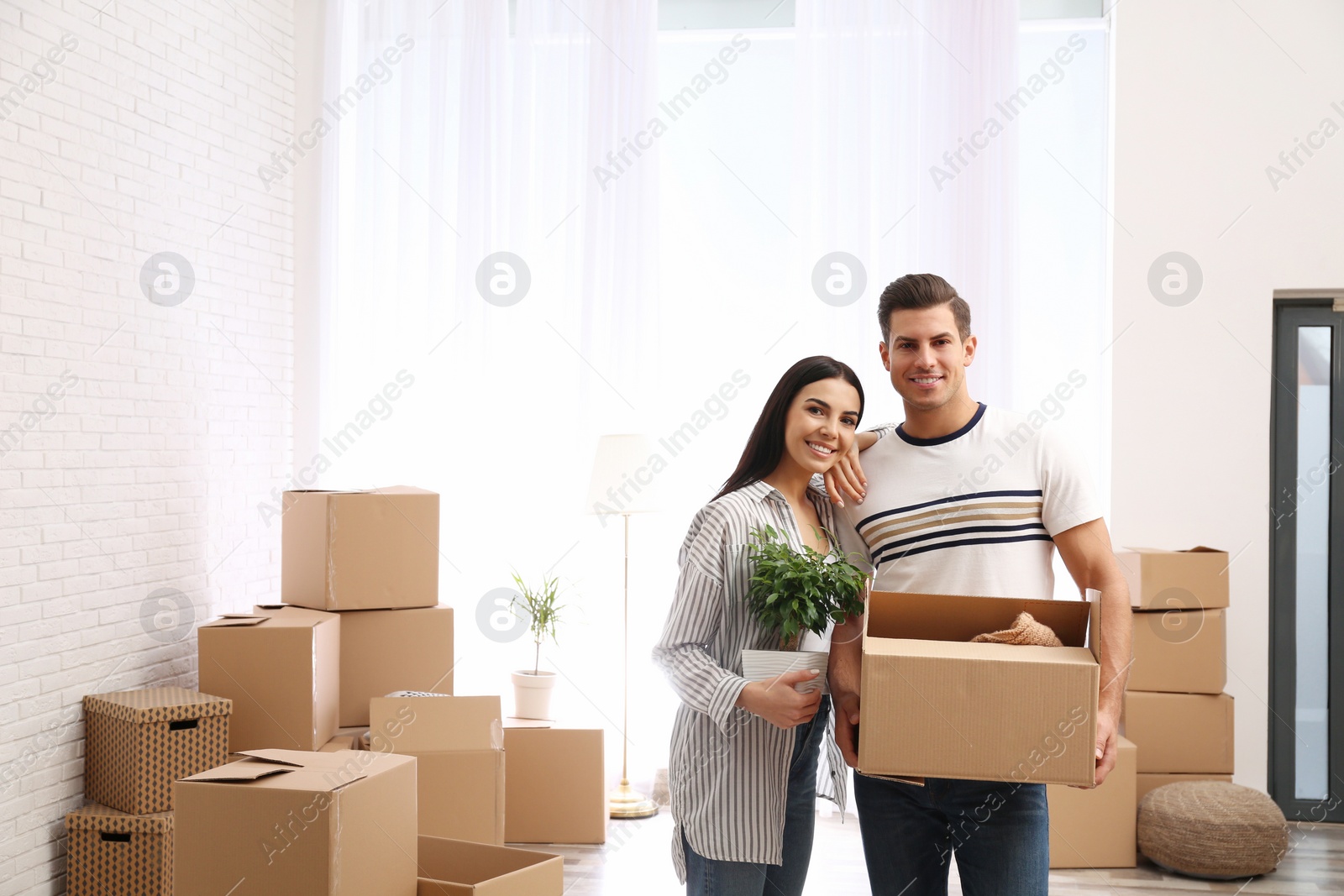 Photo of Happy couple in room with cardboard boxes on moving day