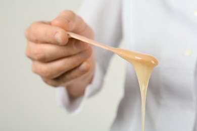 Woman holding spatula with hot depilatory wax, closeup