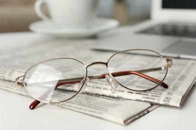 Photo of Newspapers and glasses on white table, closeup