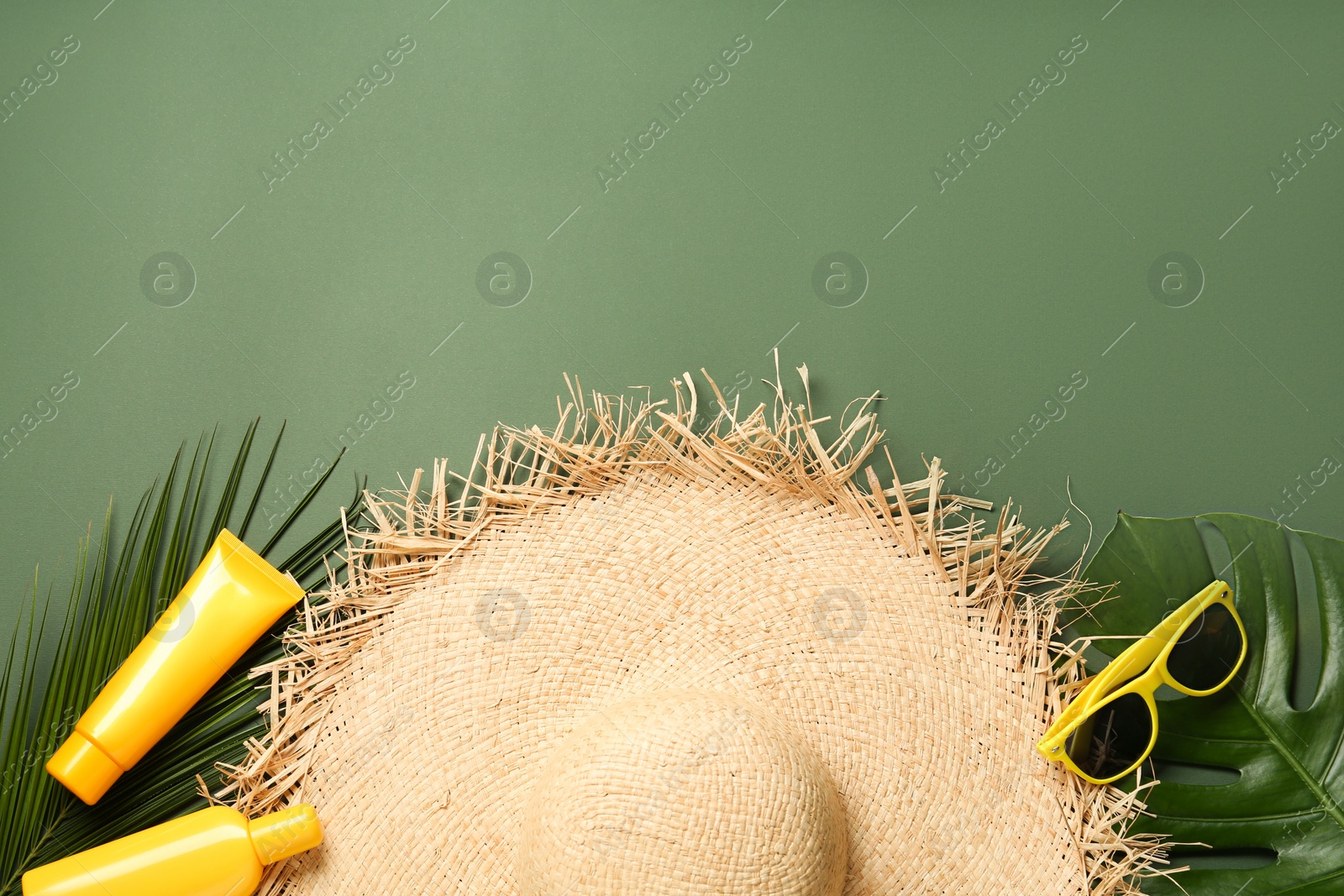 Photo of Straw hat, sunglasses, leaves, cosmetic bottles and space for text on green background, flat lay. Stylish headdress