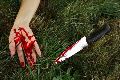 Photo of Crime scene with dead woman's body and bloody knife on green grass outdoors, closeup. Detective case