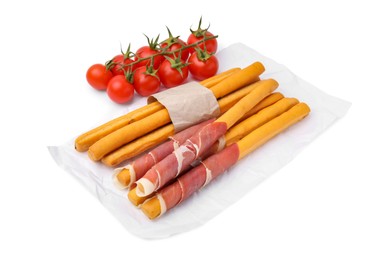 Delicious grissini sticks with prosciutto and tomatoes on white background