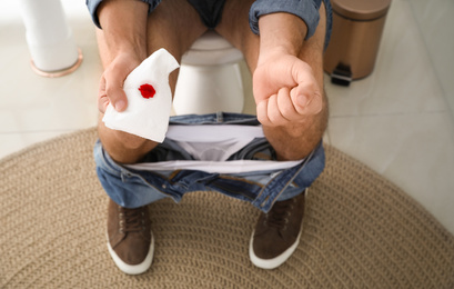 Photo of Man holding toilet paper with blood stain in rest room, closeup. Hemorrhoid concept