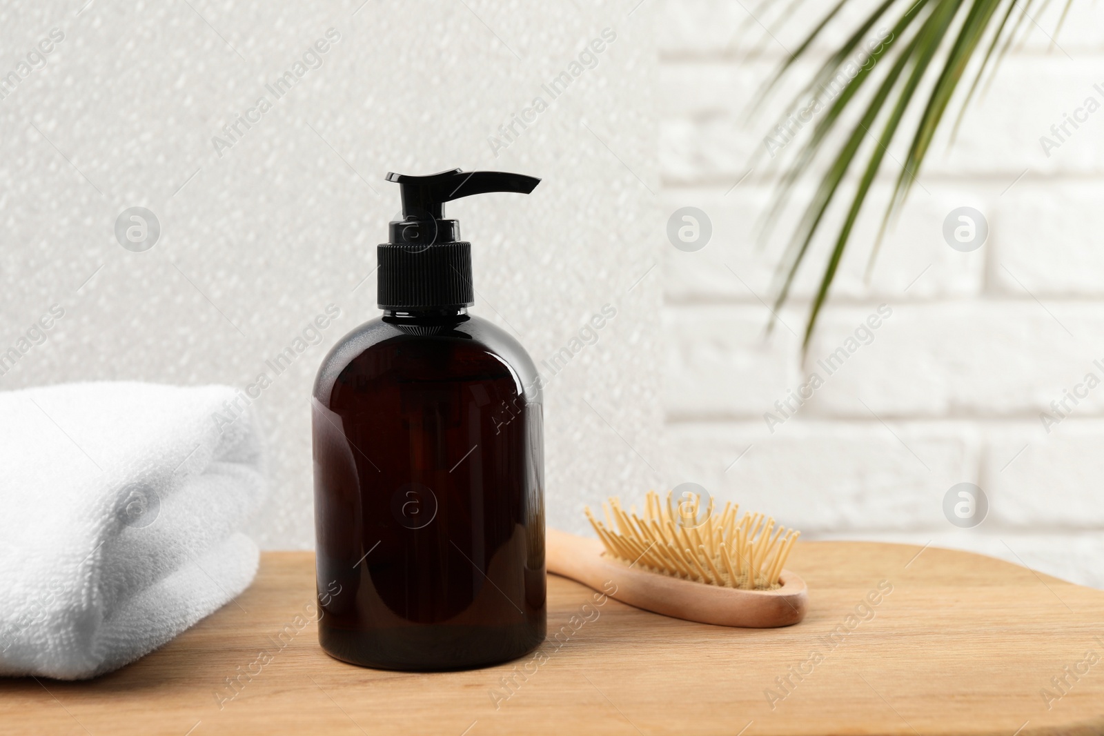 Photo of Shampoo bottle, towel and brush on wooden table