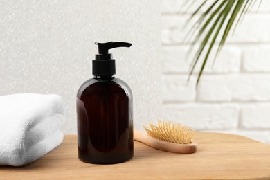 Photo of Shampoo bottle, towel and brush on wooden table