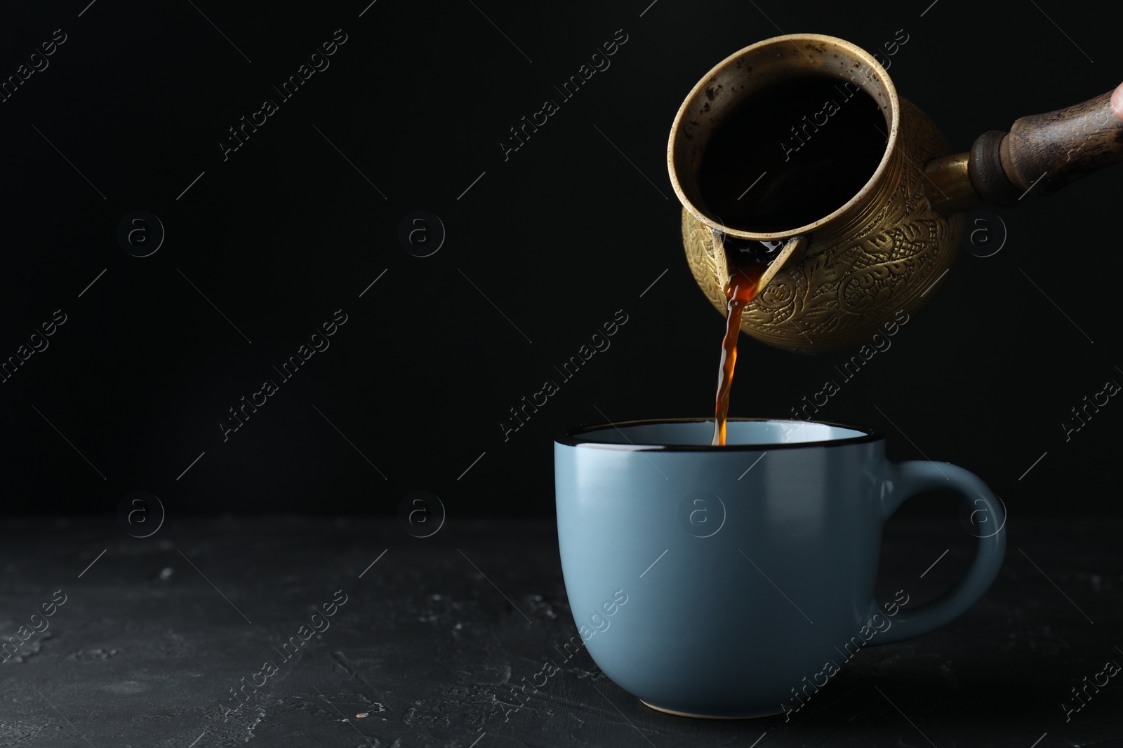 Photo of Turkish coffee. Pouring brewed beverage from cezve into cup at black table. Space for text