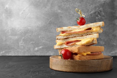 Photo of Stack of tasty sandwiches with ham and melted cheese served with tomatoes on black textured table, space for text
