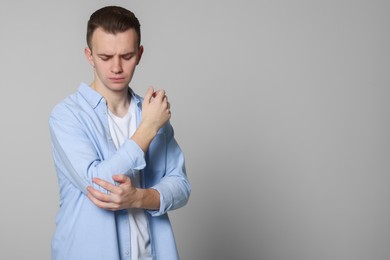 Photo of Young man suffering from pain in his elbow on light grey background, space for text. Arthritis symptoms