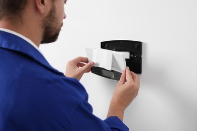 Photo of Technician installing home security alarm system on white wall indoors, closeup