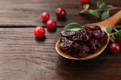 Photo of Tasty dried cranberries in spoon, fresh ones and leaves on wooden table, closeup. Space for text