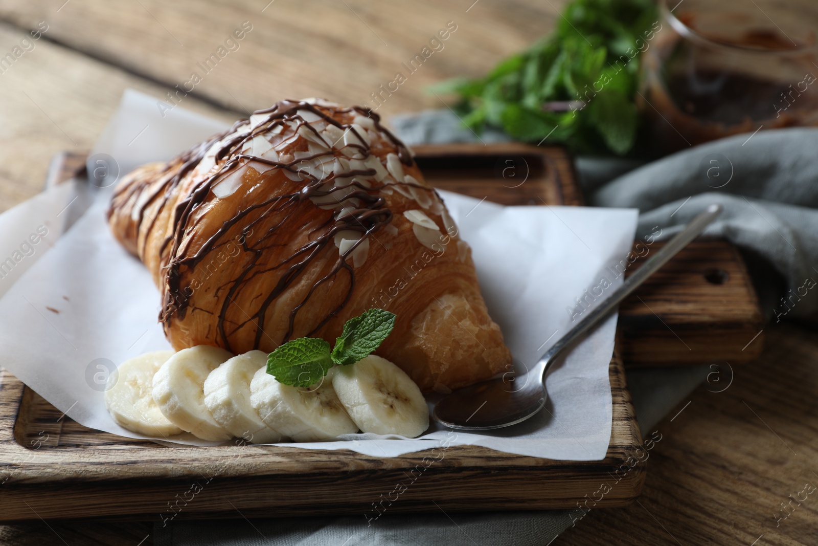 Photo of Delicious croissant with chocolate, banana and spoon on wooden table, closeup