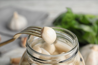 Fork with clove of pickled garlic over jar, closeup