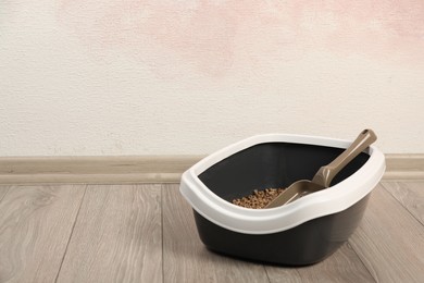 Cat tray with biodegradable litter and scoop on floor near pink wall. Space for text