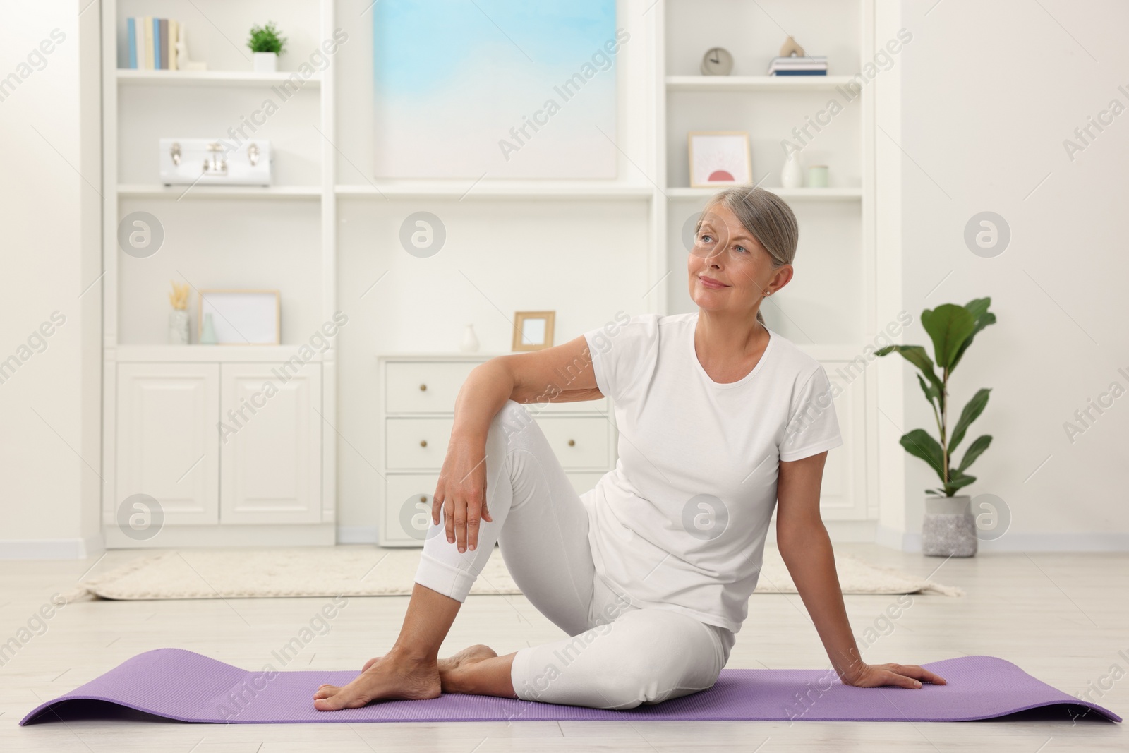 Photo of Happy senior woman sitting on mat at home. Yoga practice