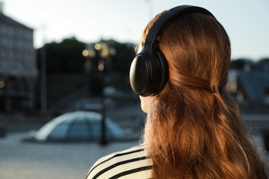 Photo of Woman in headphones listening to music on city street, back view. Space for text