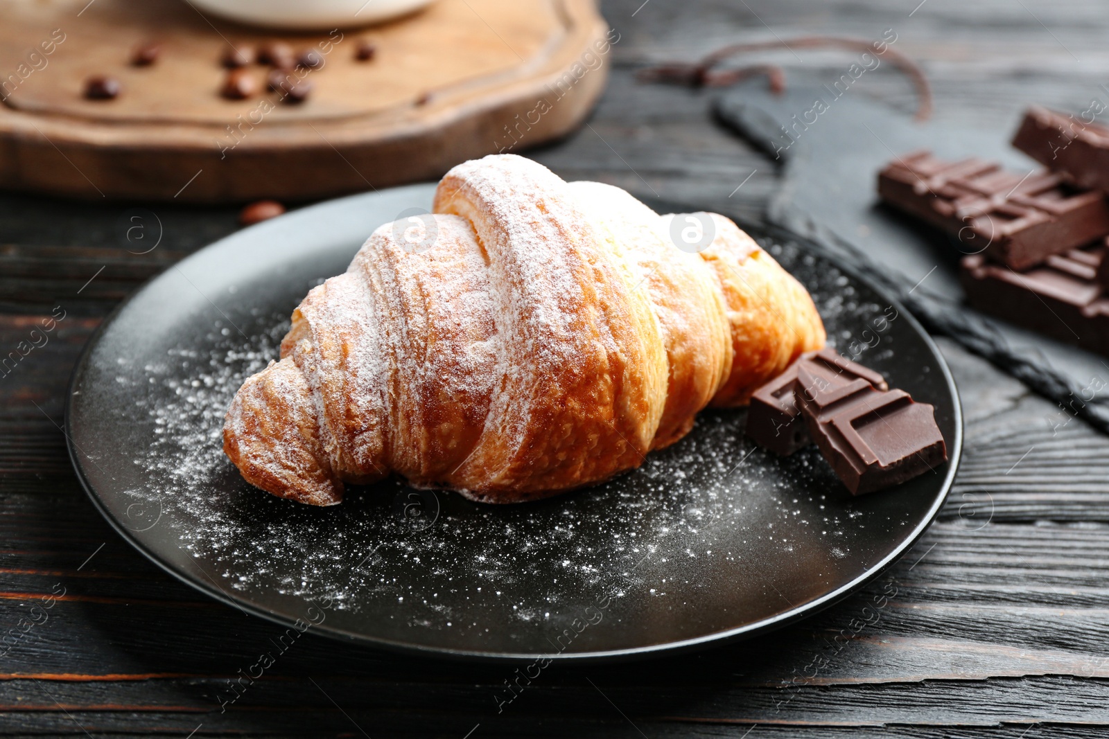 Photo of Plate of tasty croissant with powdered sugar and chocolate on dark wooden table. French pastry