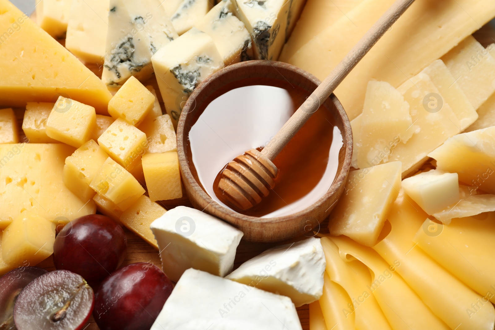 Photo of Different types of delicious cheese, grapes and honey as background, closeup