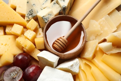 Different types of delicious cheese, grapes and honey as background, closeup