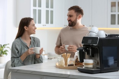 Photo of Happy couple enjoying fresh aromatic coffee in kitchen, focus on modern machine