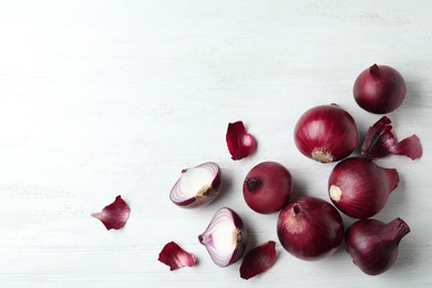Photo of Ripe red onions and peels on white wooden table, top view with space for text