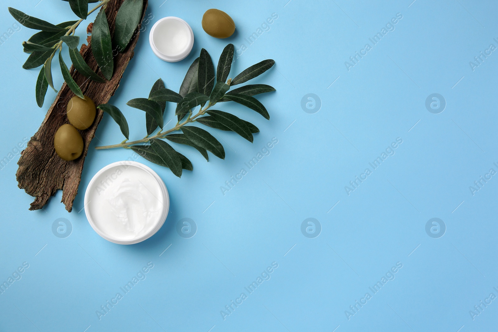 Photo of Flat lay composition with jars of cream and olives on light blue background. Space for text