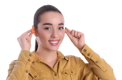 Young woman inserting foam ear plugs on white background