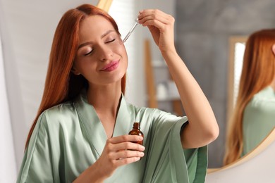 Beautiful young woman applying cosmetic serum onto her face in bathroom