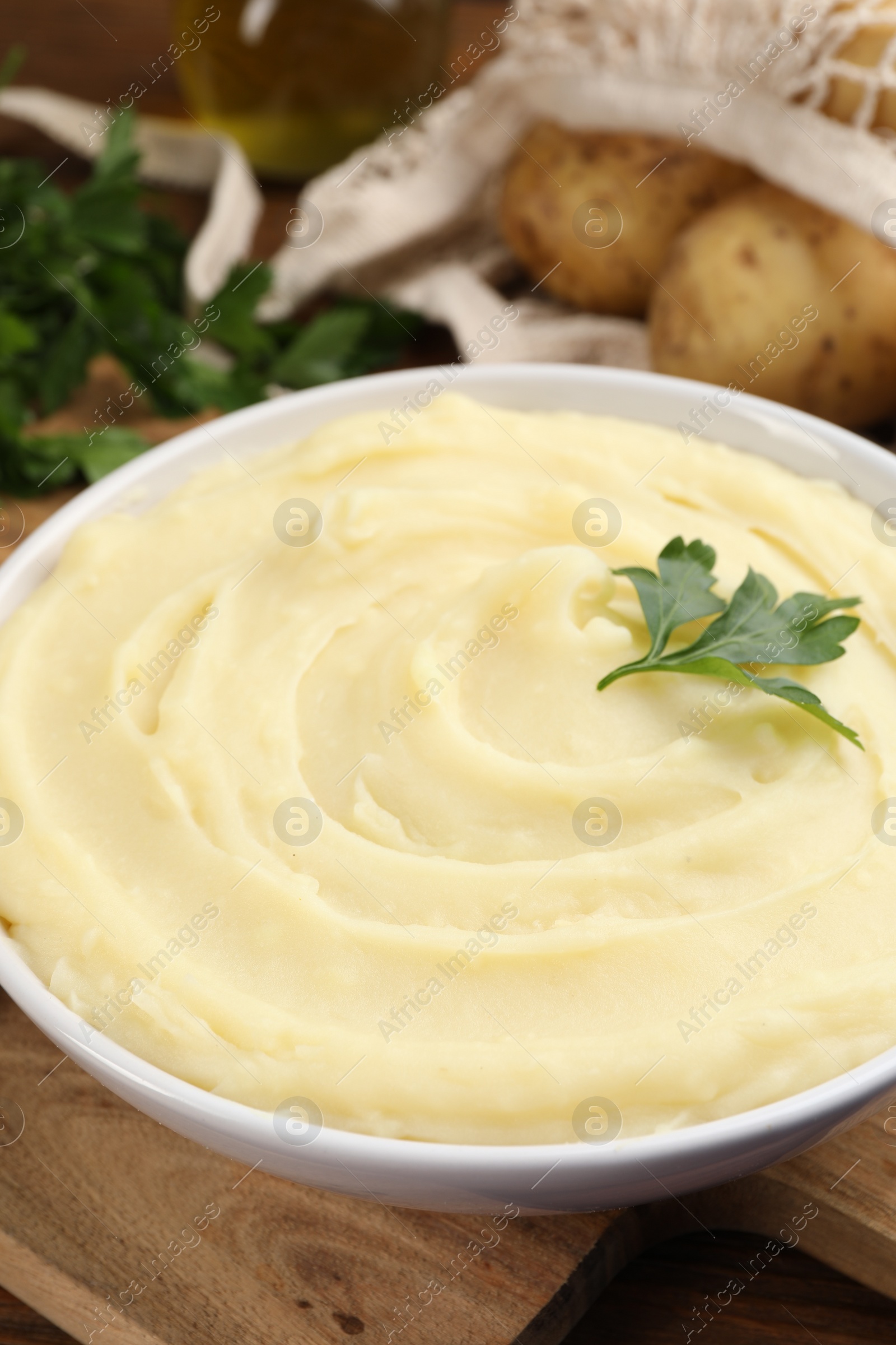 Photo of Bowl of tasty mashed potato and parsley on wooden table, closeup