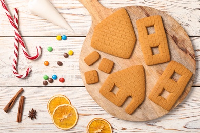 Parts of gingerbread house and ingredients for decoration on white wooden table, flat lay