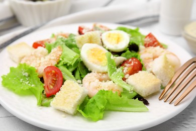 Photo of Delicious Caesar salad with shrimps and fork served on table, closeup