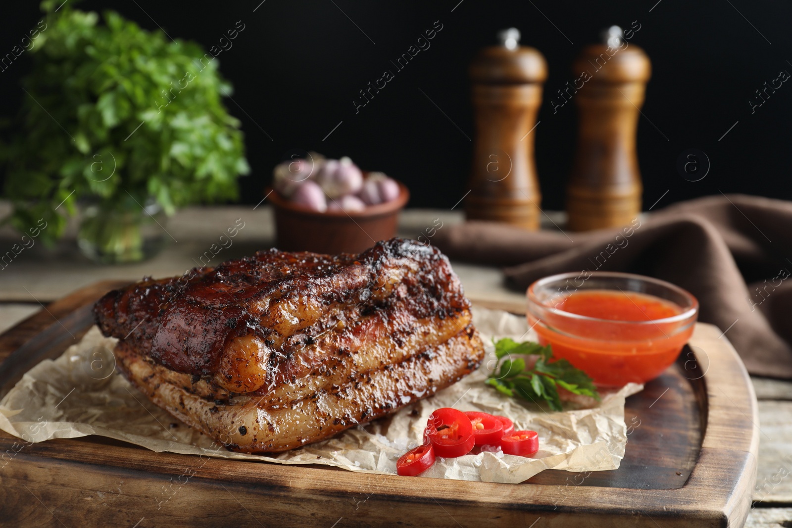 Photo of Piece of baked pork belly served with sauce and chili pepper on wooden board