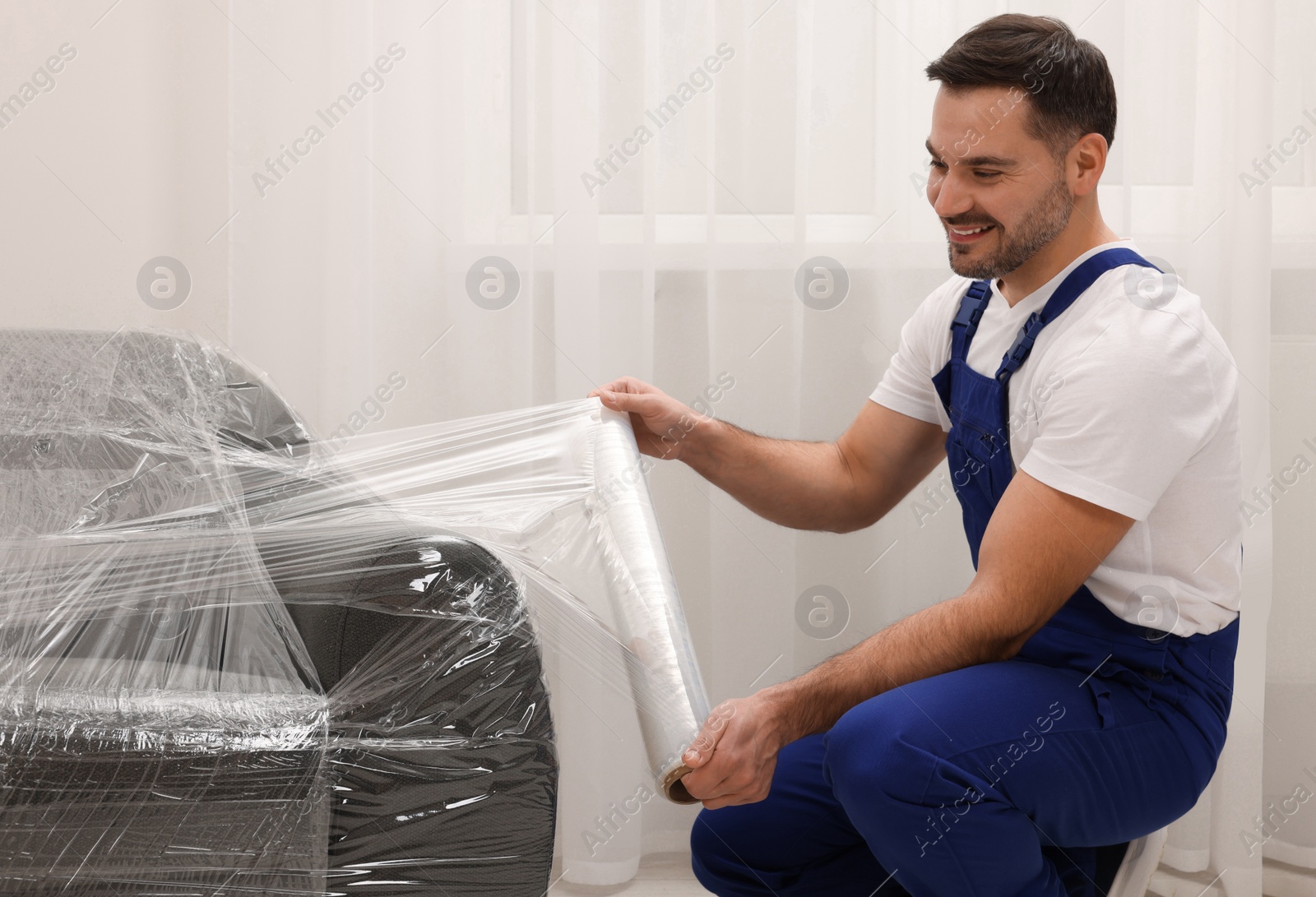 Photo of Worker wrapping sofa in stretch film indoors