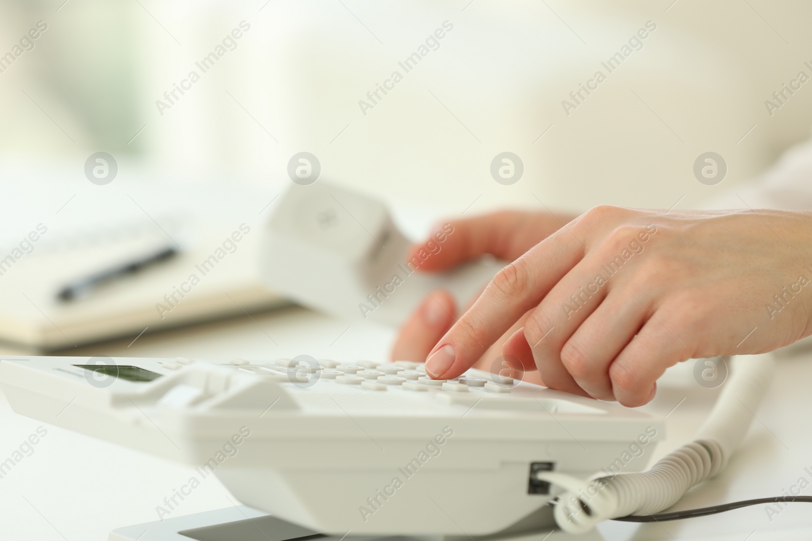 Photo of Assistant dialing number on telephone at white table, closeup