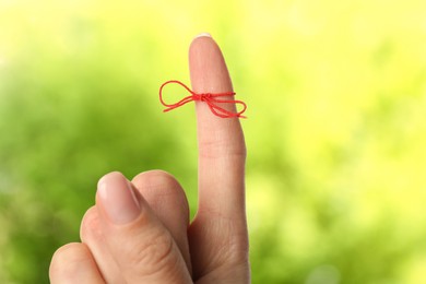 Woman showing index finger with tied red bow as reminder on blurred green background, closeup