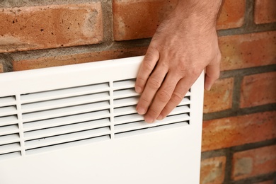 Man checking temperature of heating convector on brick, closeup