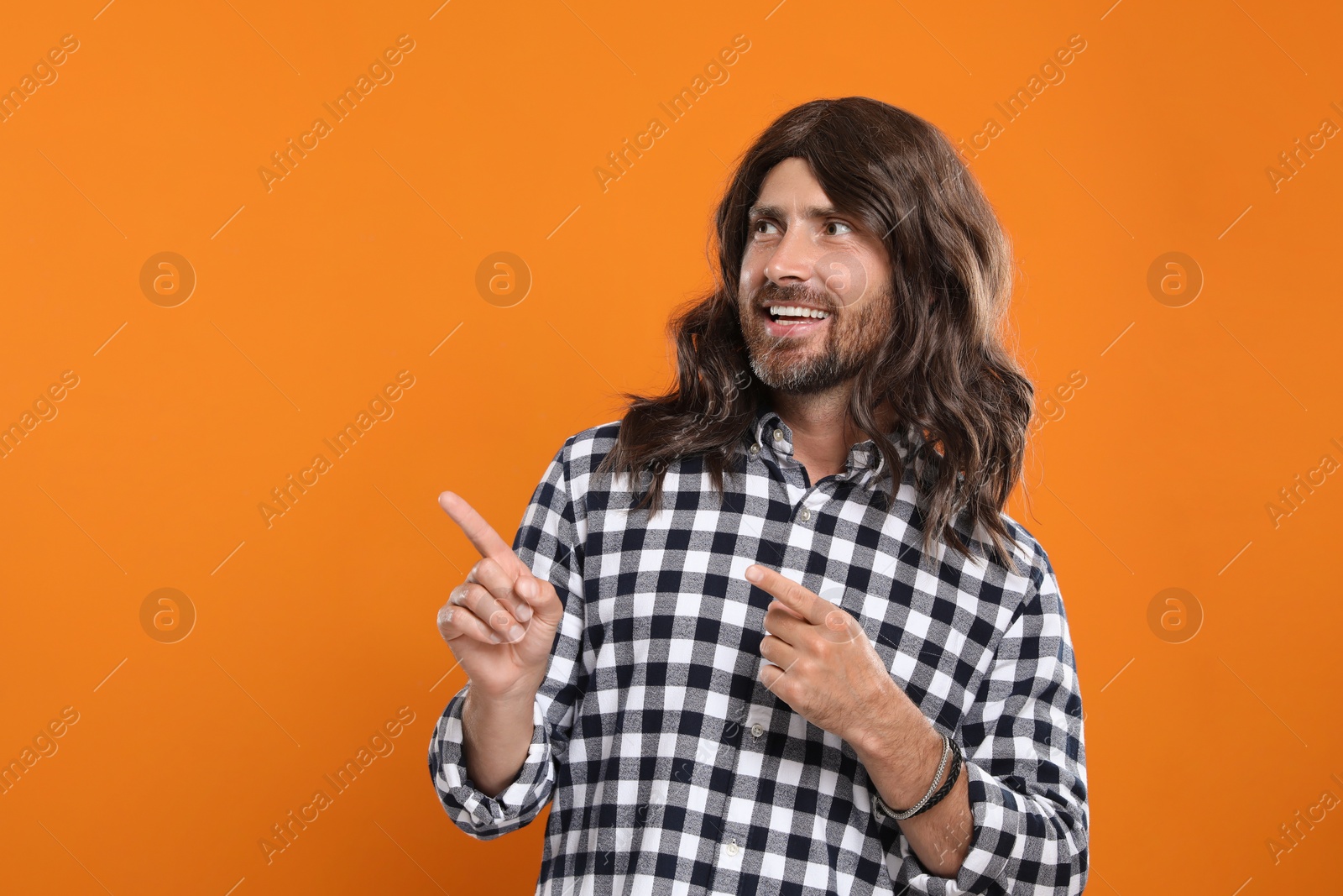 Photo of Hippie man pointing at something on orange background, space for text
